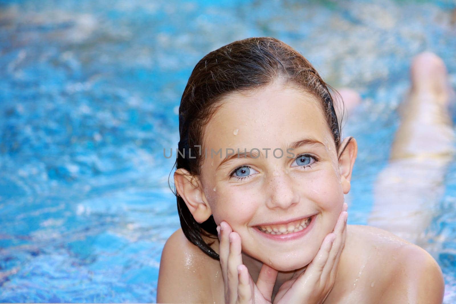 a blue eyed girl lying in a swimming pool smiling at the camera with her hands cupped into her chin