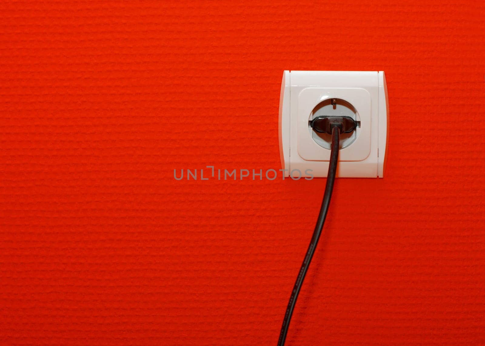 Electric outlet on red wall with cable connected