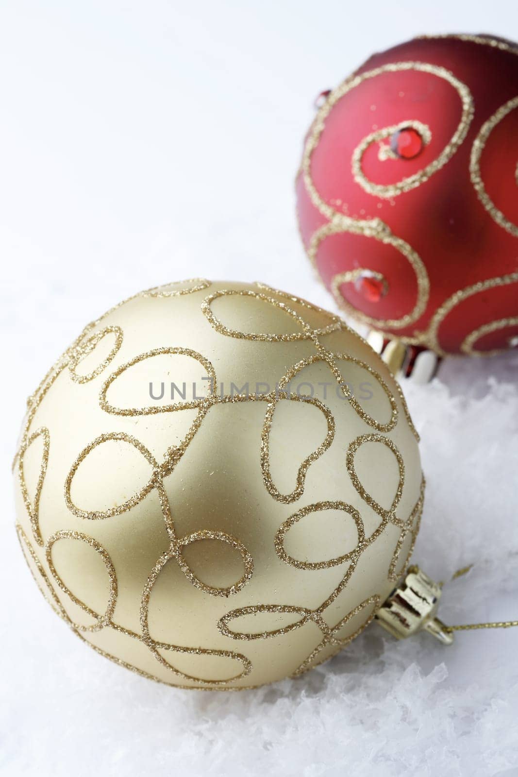 A close-up of two, red and gold colored, Christmas bauble decorations resting on white snowflakes.