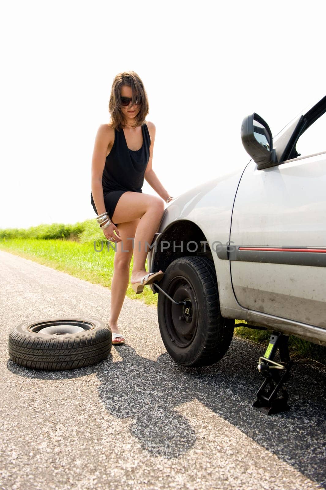 Sexy brunette aggressively kicking the wrench to tighten the nuts of a flat tire she just replaced