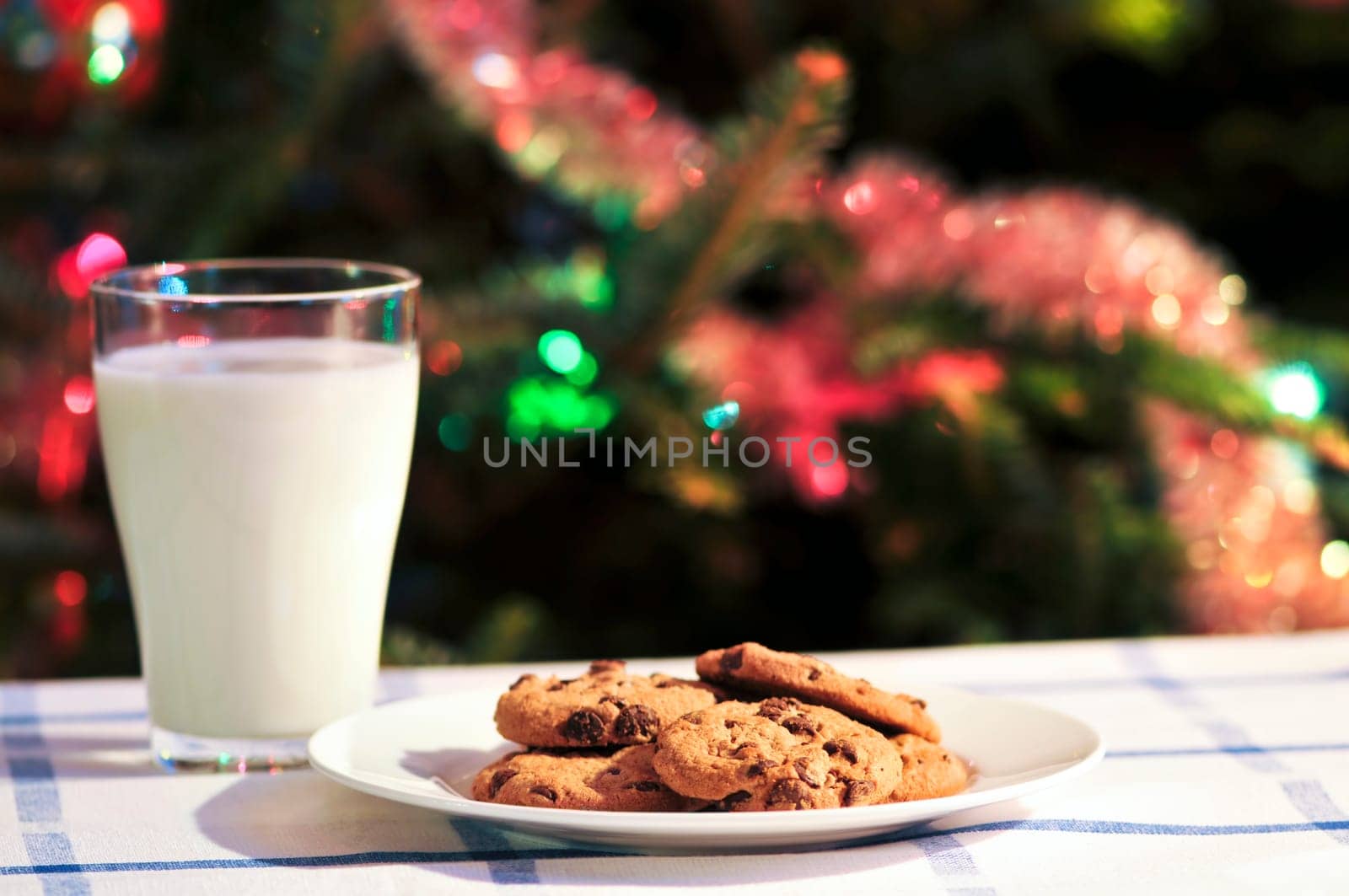 Plate of cookies and glass of milk near Christmas tree
