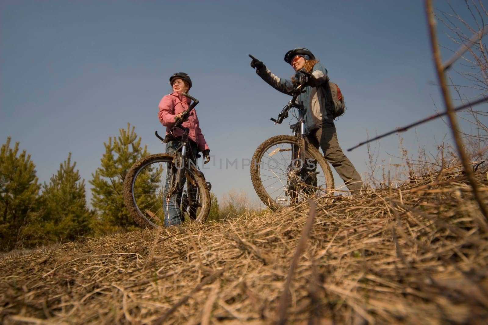 Two women-bikers standing. Shot from below