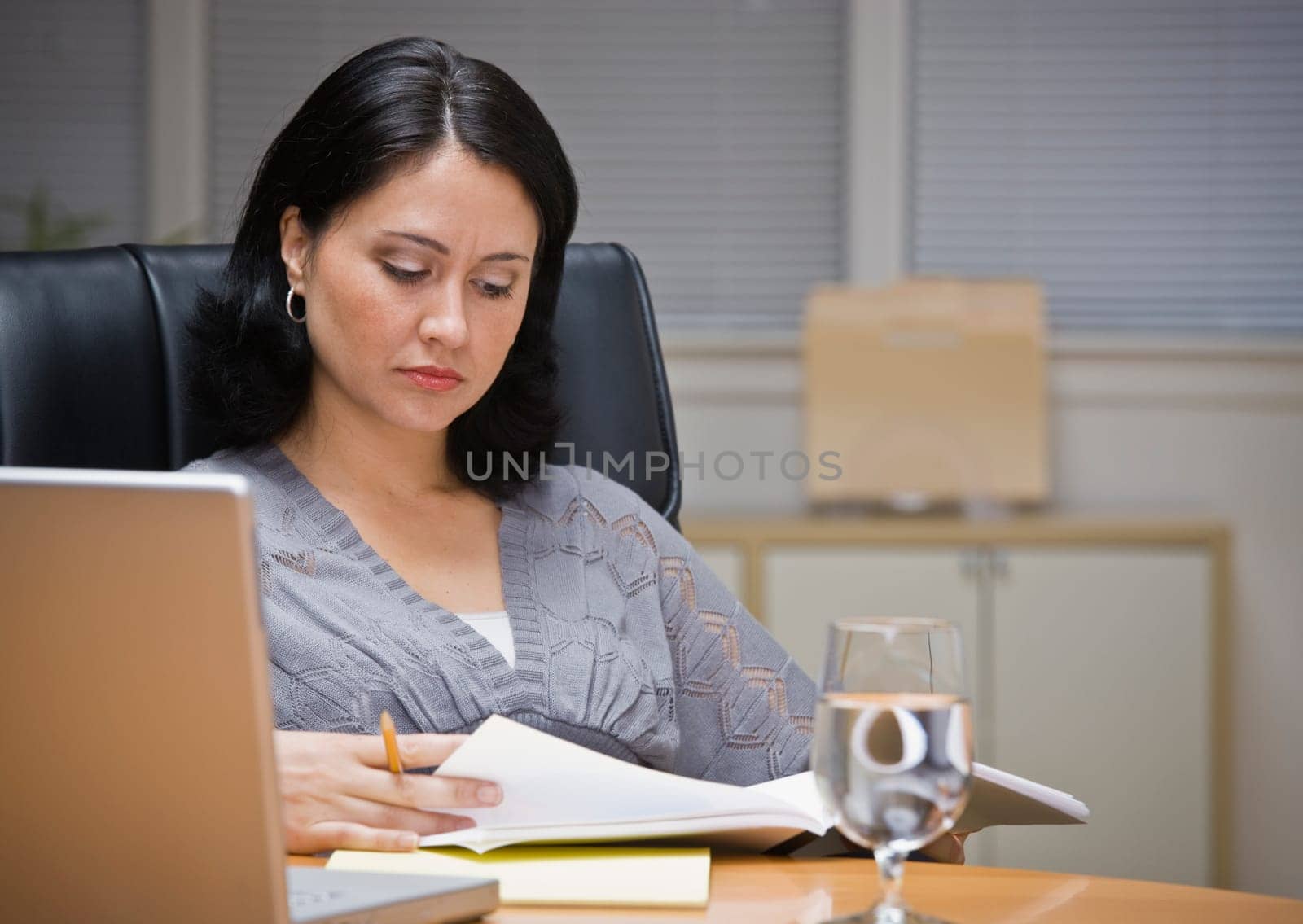 A young businesswoman is seated at a desk in an office.  She is looking away from the camera.  Horizontally framed shot.