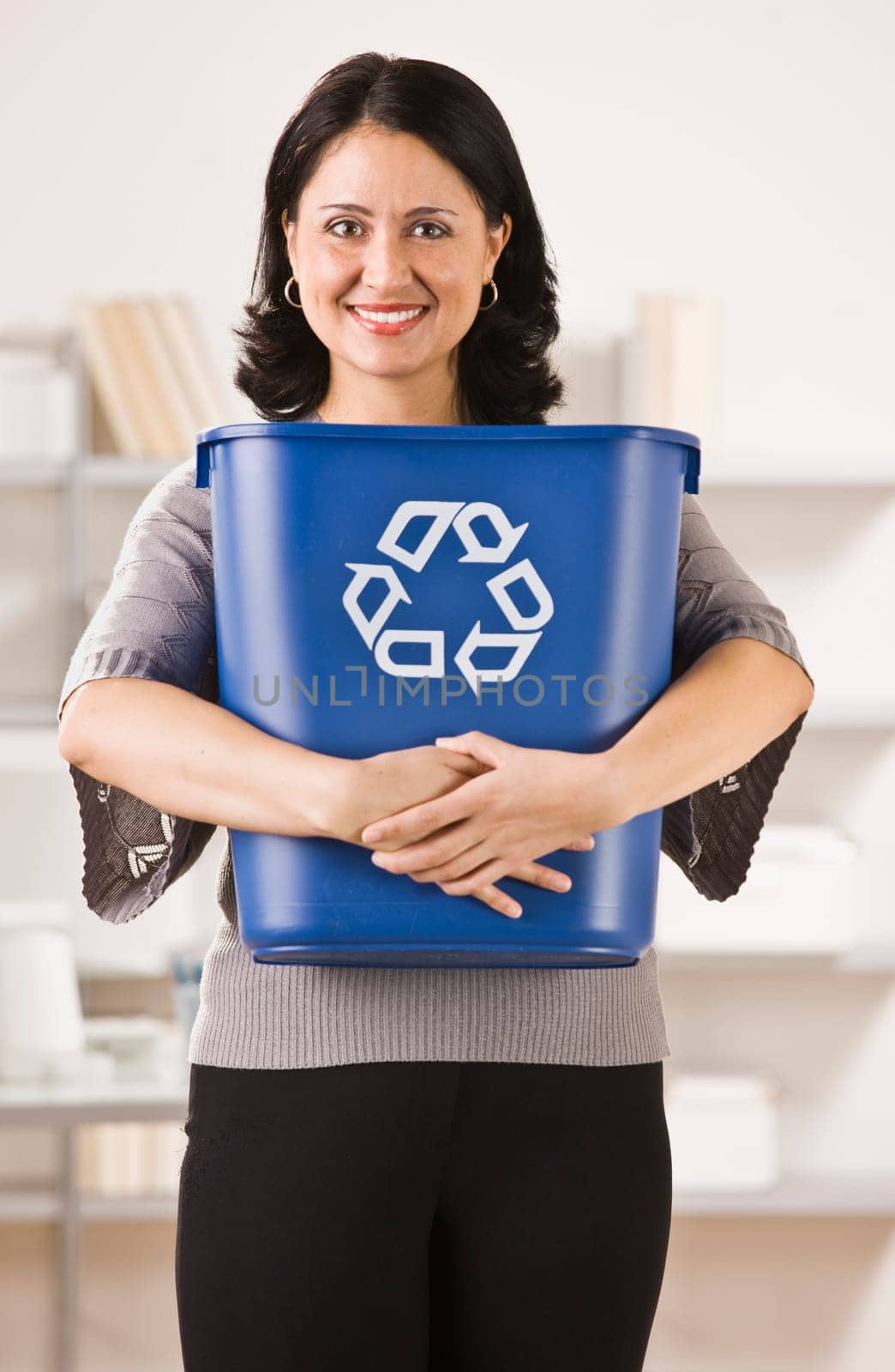 A businesswoman is holding a recycling basket and smiling at the camera.  Vertically framed shot.