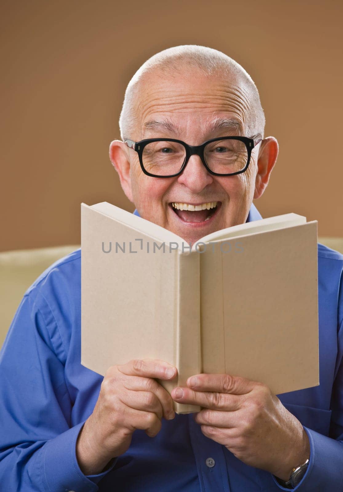 Laughing senior male reading a book on a couch. Vertical