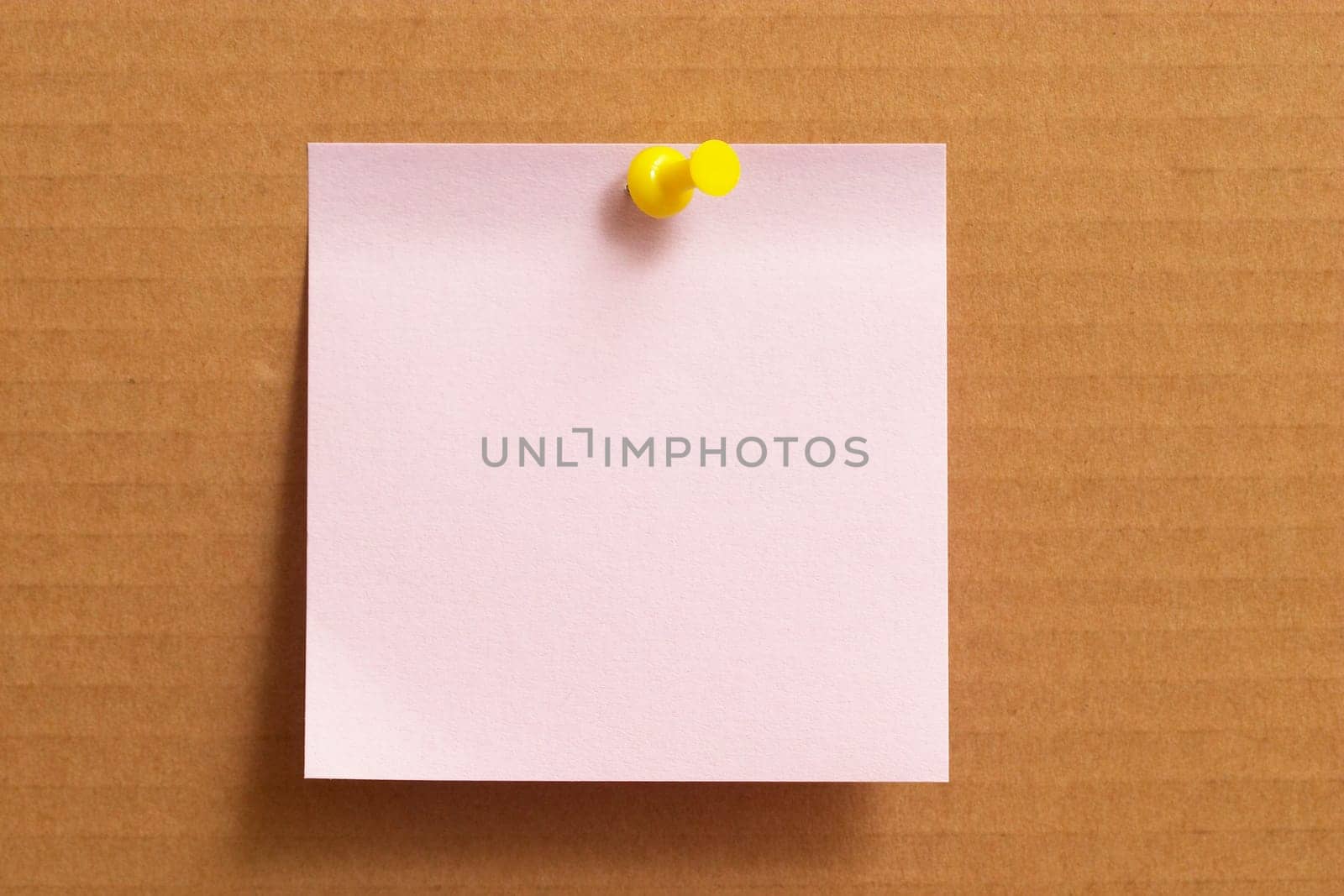 Pink sticker note with yellow push-pin on cardboard