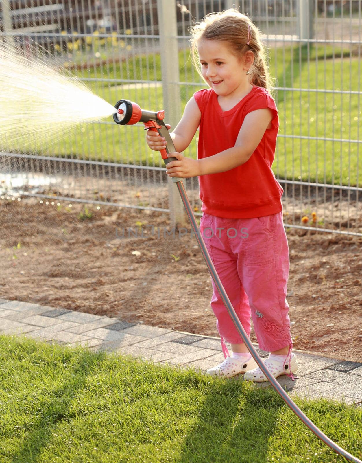 Little girl watering the grass in the garden