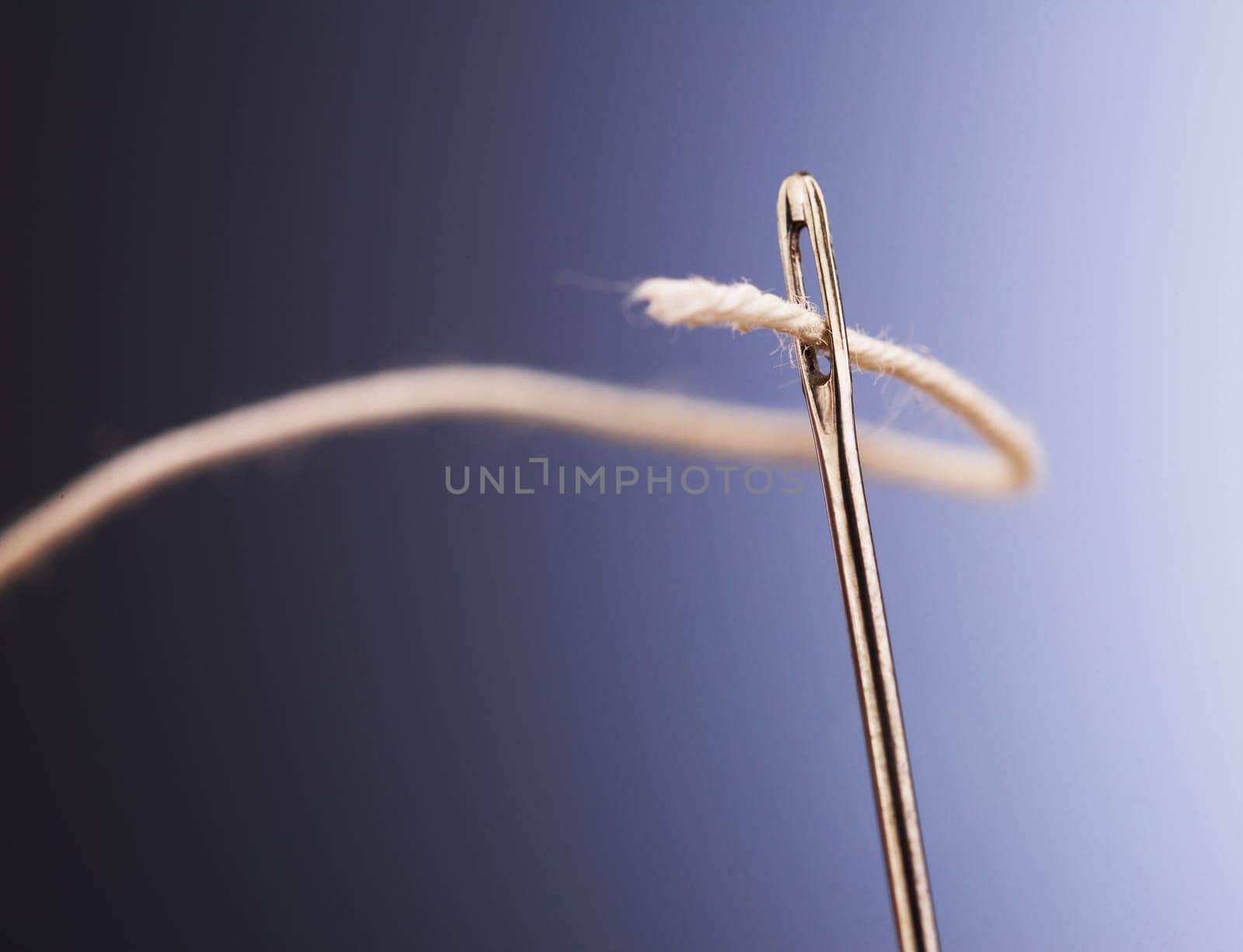 White thread going through needle eye, closeup
