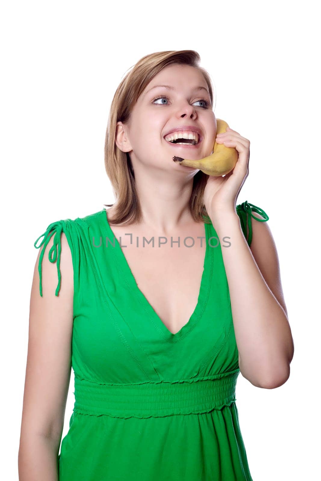 Pretty girl in a green dress is holding a banana as a phone, isolated on white