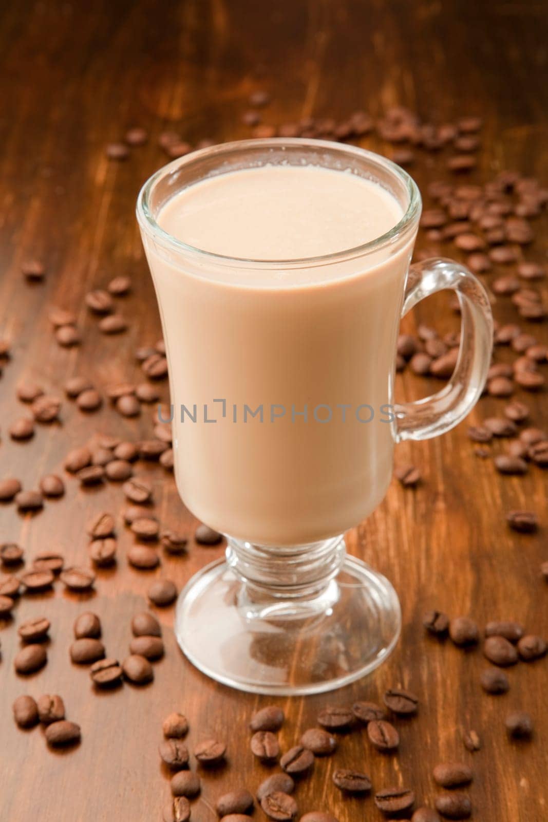 Arabica espresso beans around a glass mug of caffe latte.