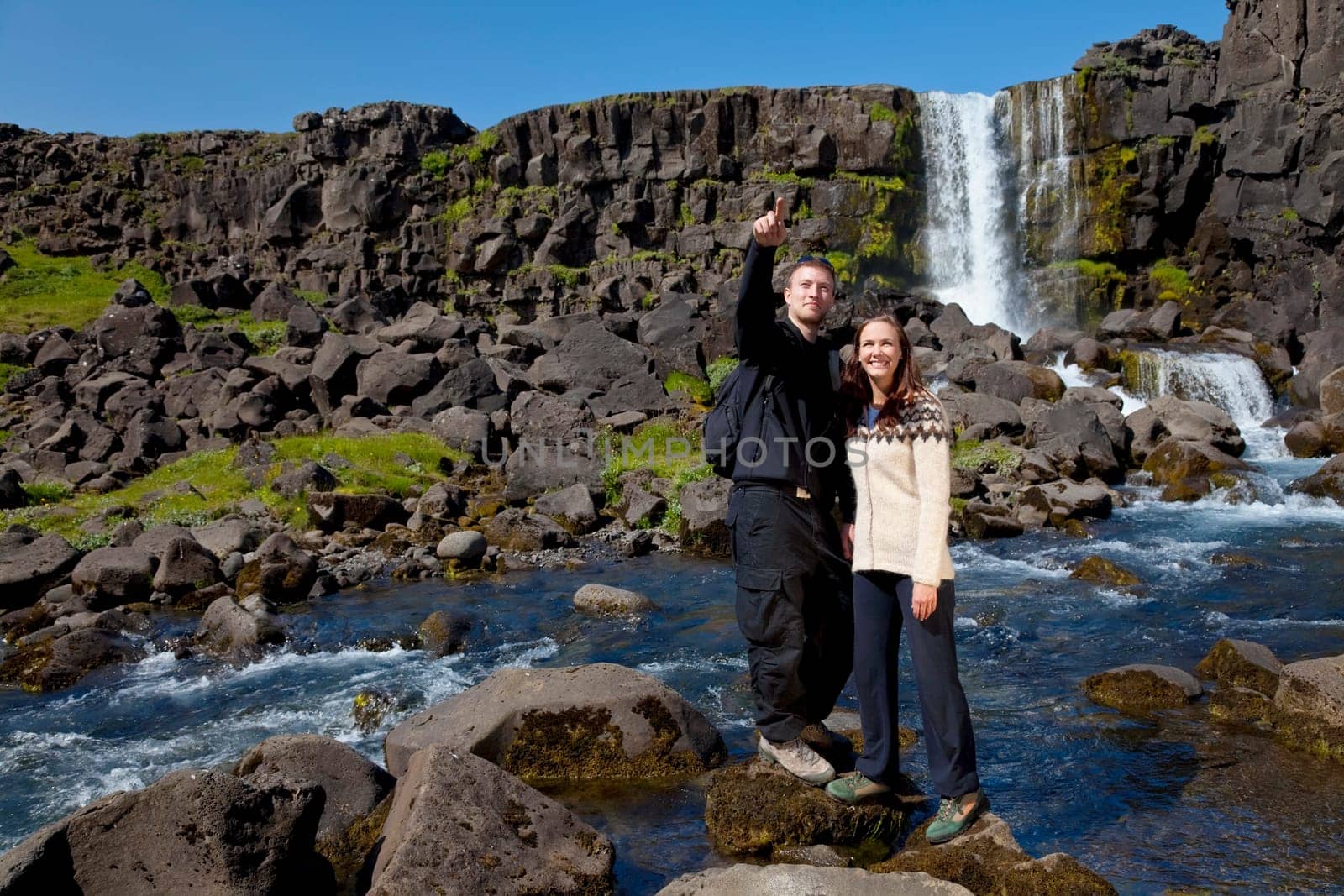 A young couple crossing a mountain stream while out walking together. Shot on location in Iceland.