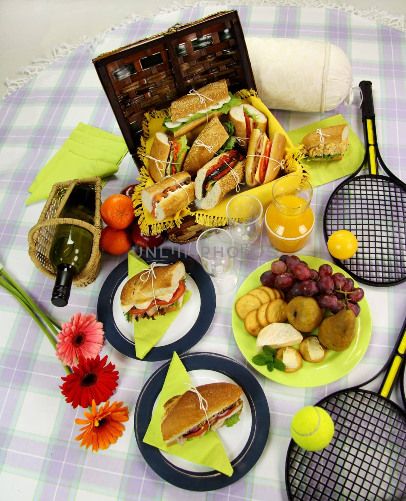 Selection of food for a picnic with a hamper, basket, fruit, wine and tennis racquets.