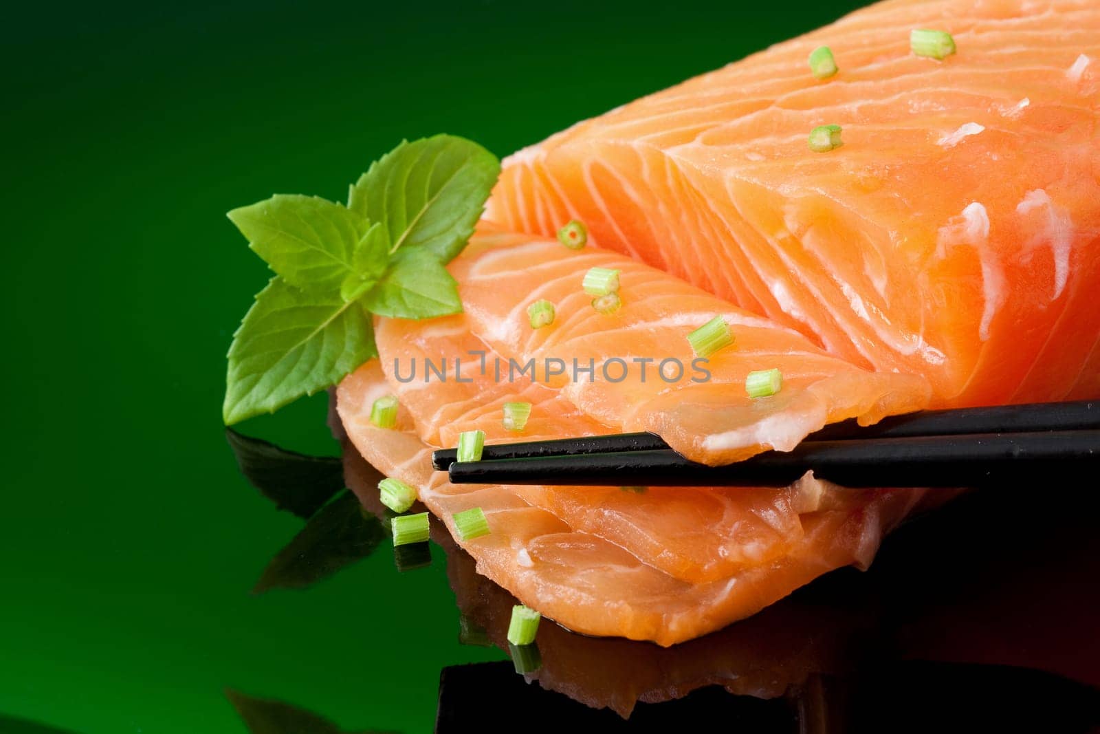 a piece of fresh salmon with basil leaves and chopstick