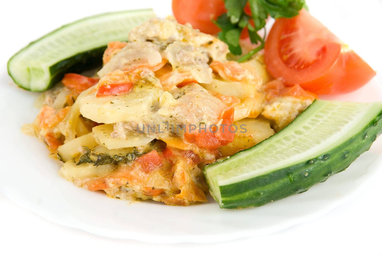 Close up of meat, potatoes, tomatoes and cucumbers dish on white