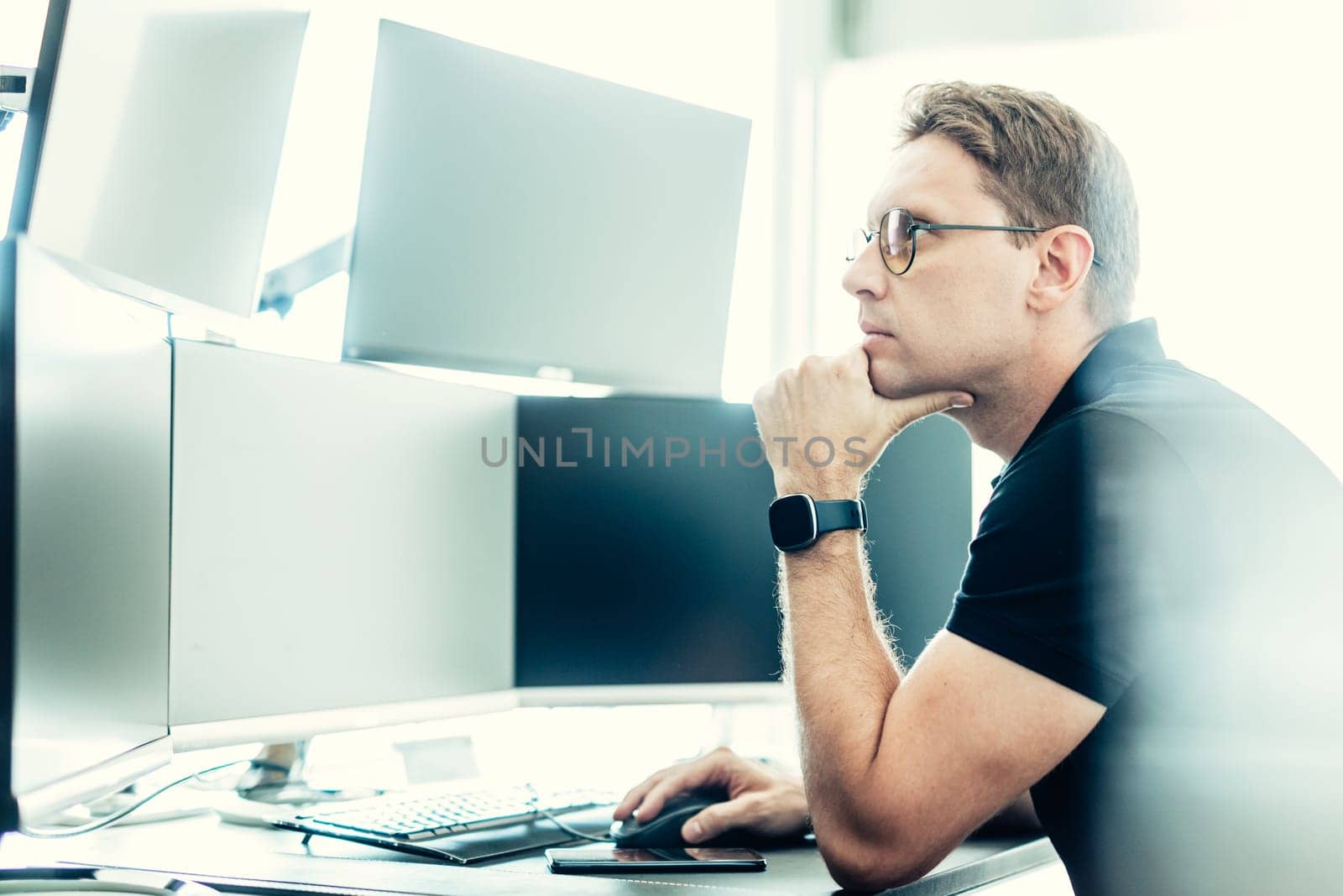 Male stock broker trading online watching charts and data analyses on multiple computer screens.