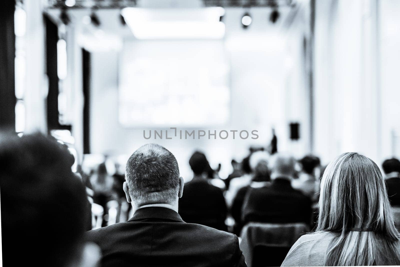 Speaker giving a talk in conference hall at business event. Rear view of unrecognizable people in audience at conference hall. Business and entrepreneurship concept. Black and white selenium image.