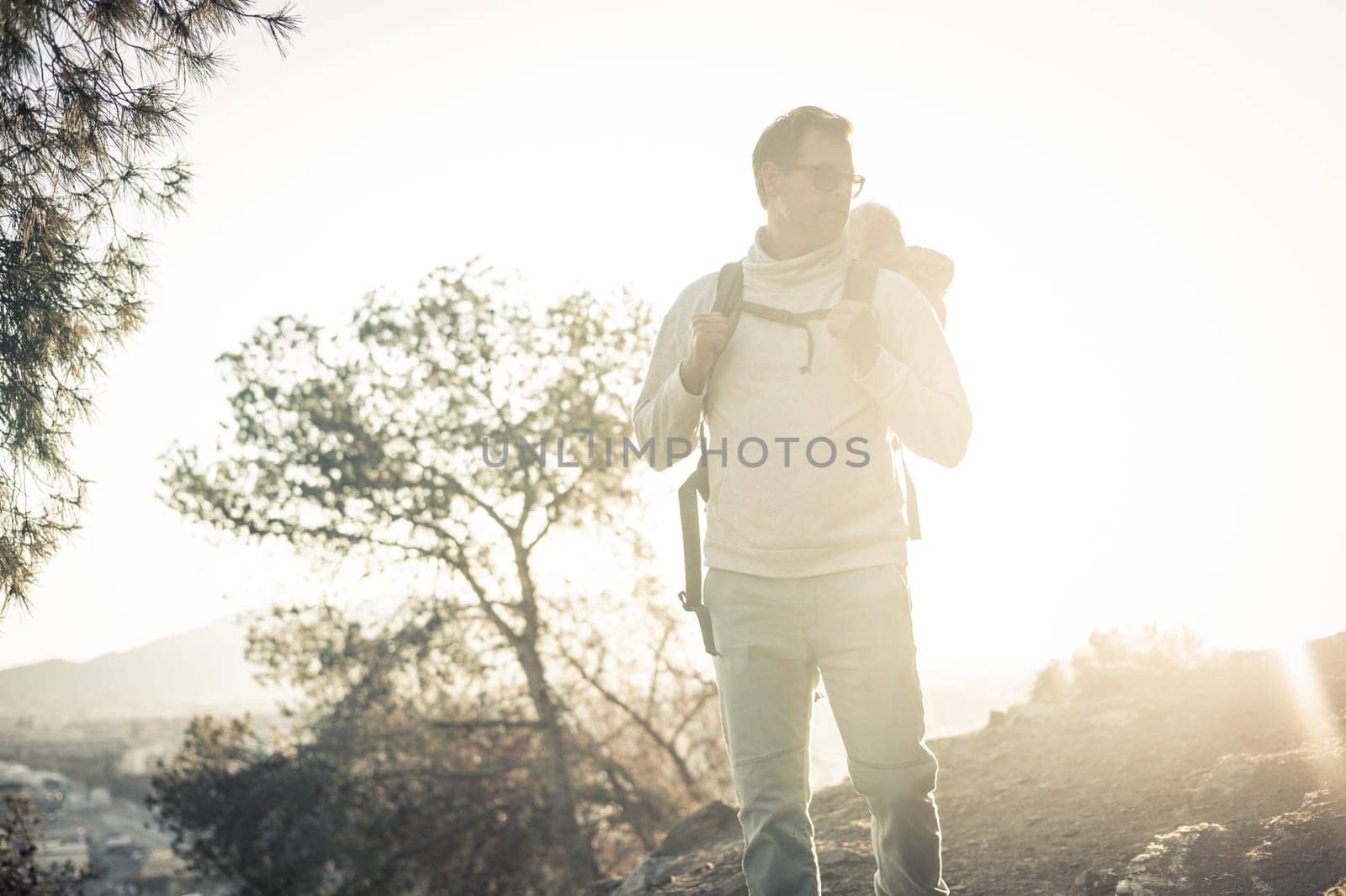Young father carrying his infant baby boy son in backpack while tracking around Malaga, Spain in sunset. Family travel and vacation concept.