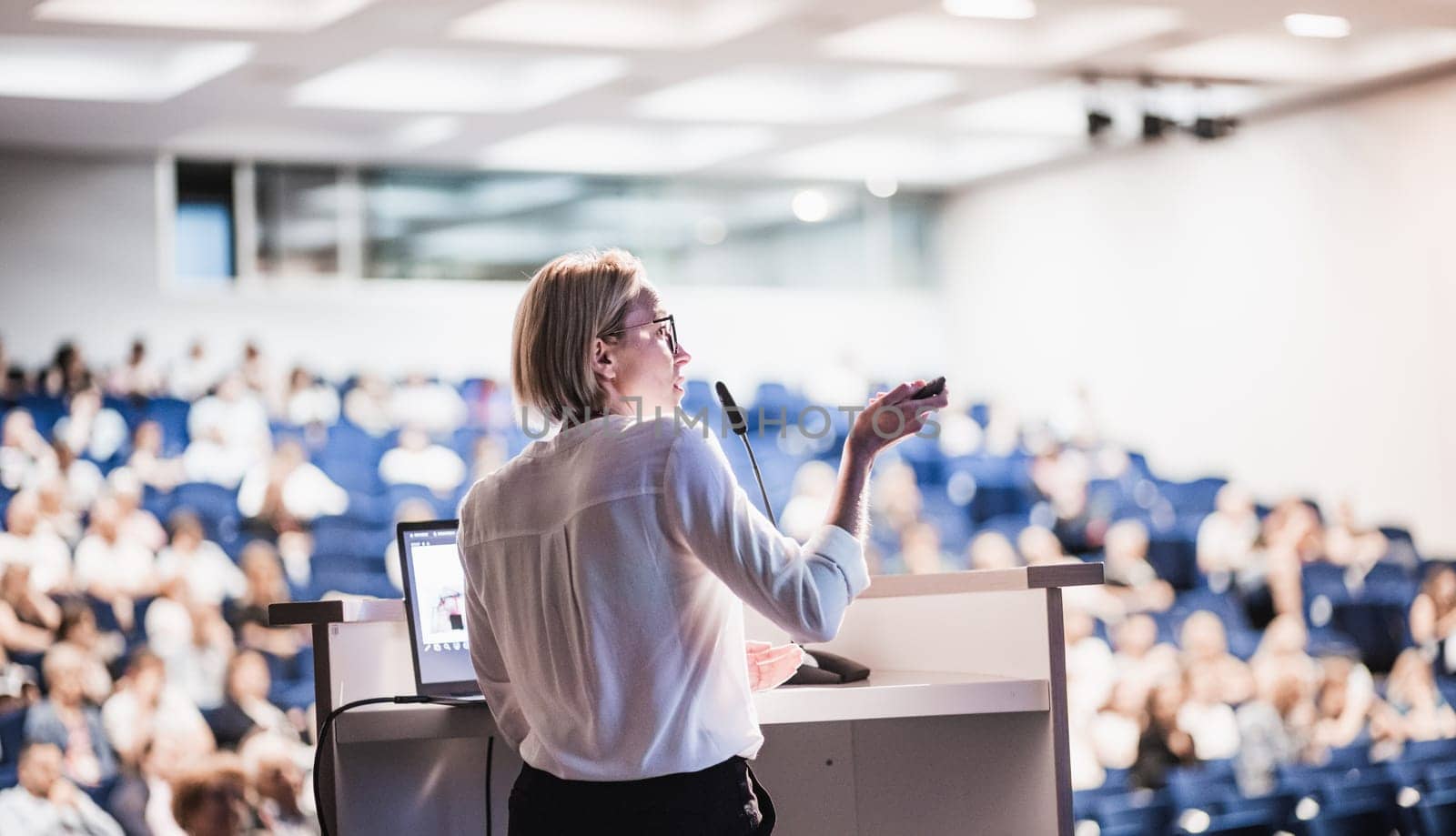 Female speaker giving a talk on corporate business conference. Unrecognizable people in audience at conference hall. Business and Entrepreneurship event