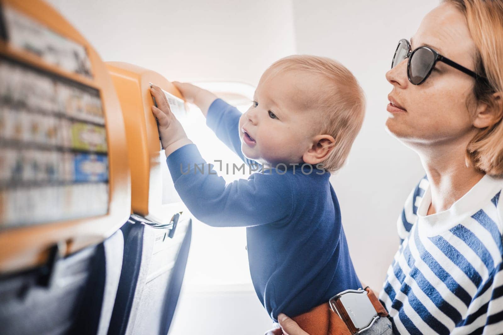 Mom and child flying by plane. Mother holding and playing with her infant baby boy child in her lap during economy comercial flight. Concept photo of air travel with baby. Real people