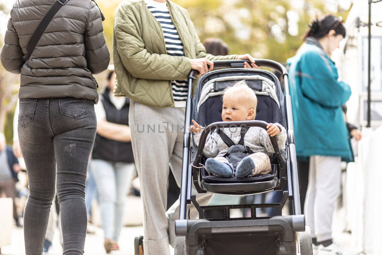 Mother walking and pushing his infant baby boy child in stroller in crowd of people wisiting sunday flea market in Malaga, Spain