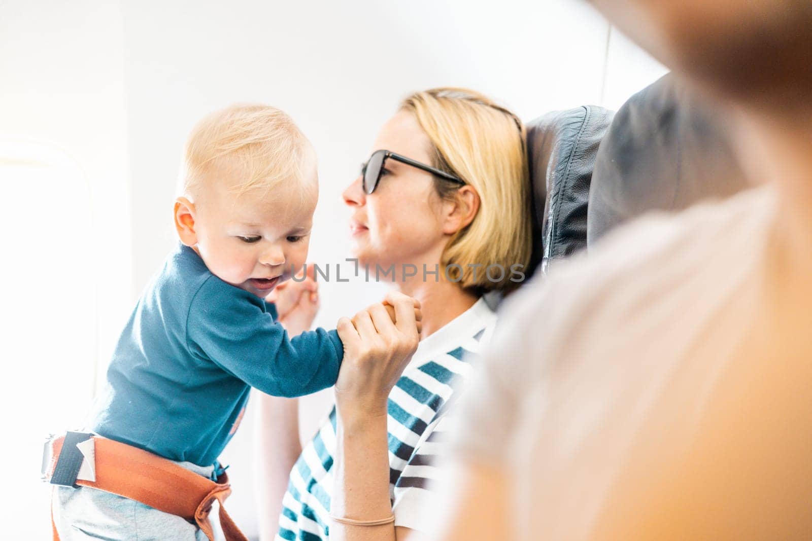 Mom and child flying by plane. Mother holding and playing with her infant baby boy child in her lap during economy comercial flight. Concept photo of air travel with baby. Real people