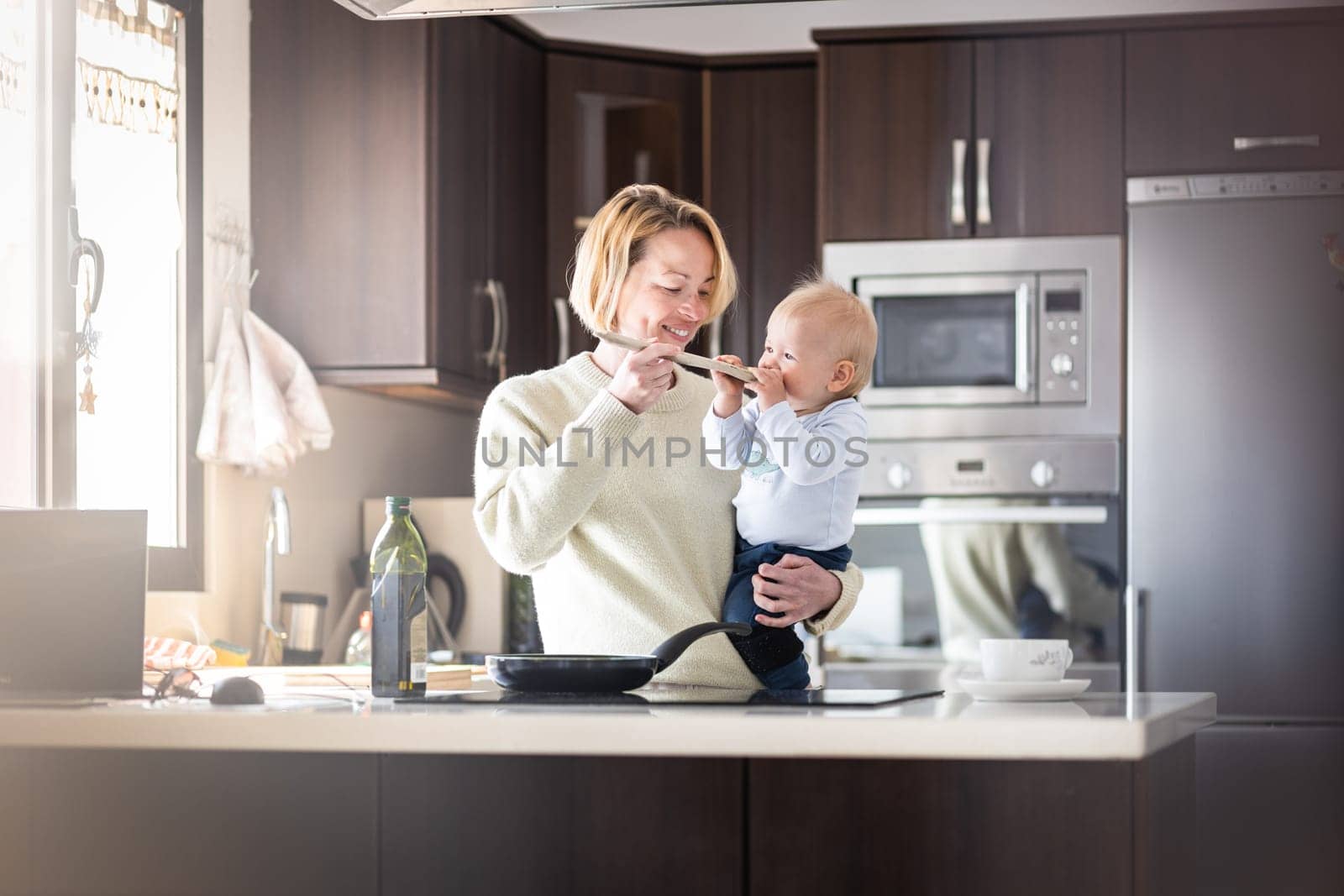 Happy mother and little infant baby boy cooking and tasting healthy dinner in domestic kitchen. Family, lifestyle, domestic life, food, healthy eating and people concept