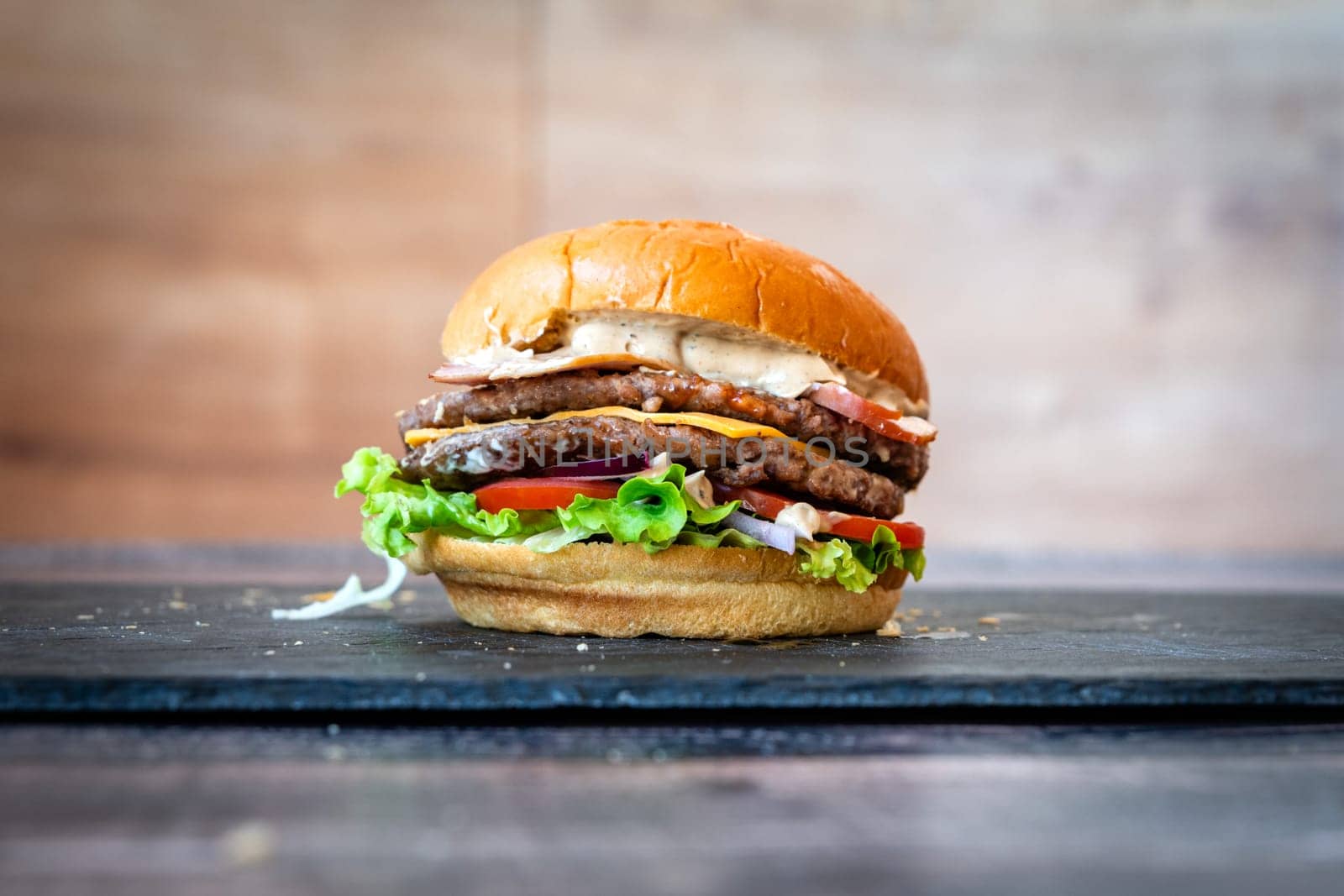 beef burger with sesame lettuce bun tomato cheddar cheese on black background