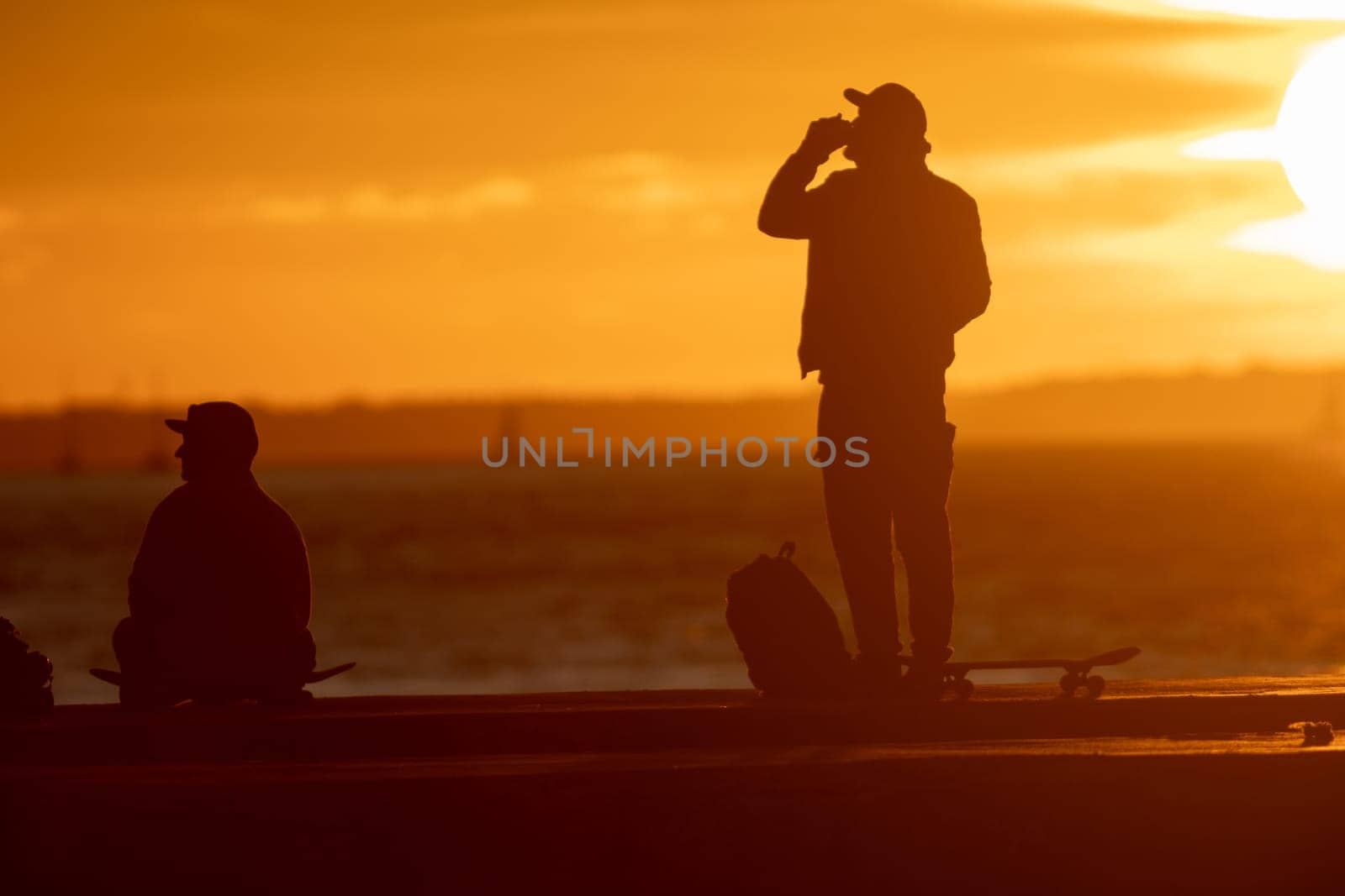 Young skateboarders hanging out on the waterfront at sunset. Mid shot