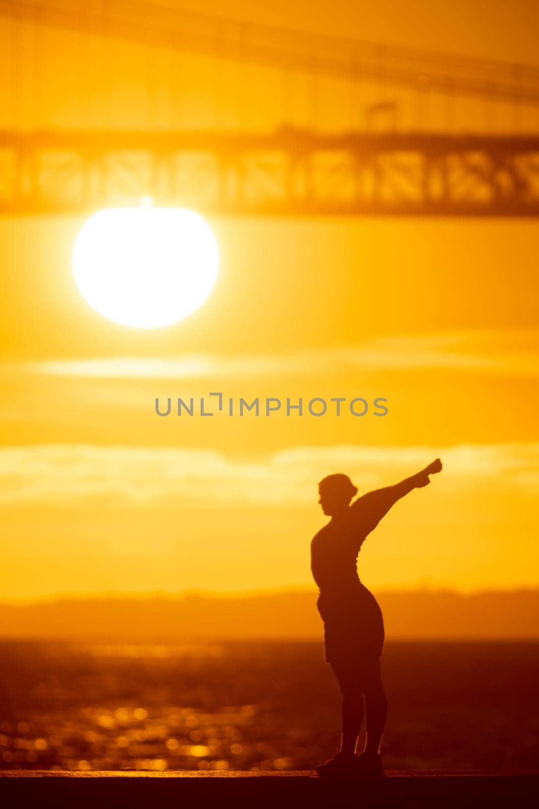 A sporty man stretching out on the waterfront at sunset. Mid shot