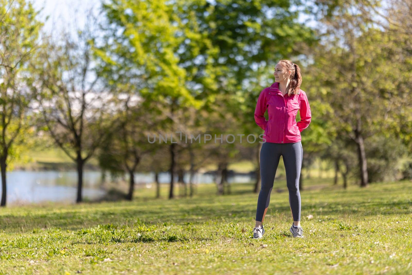An adult smiling woman in sports clothes standing on the field and looking to the side. Mid shot