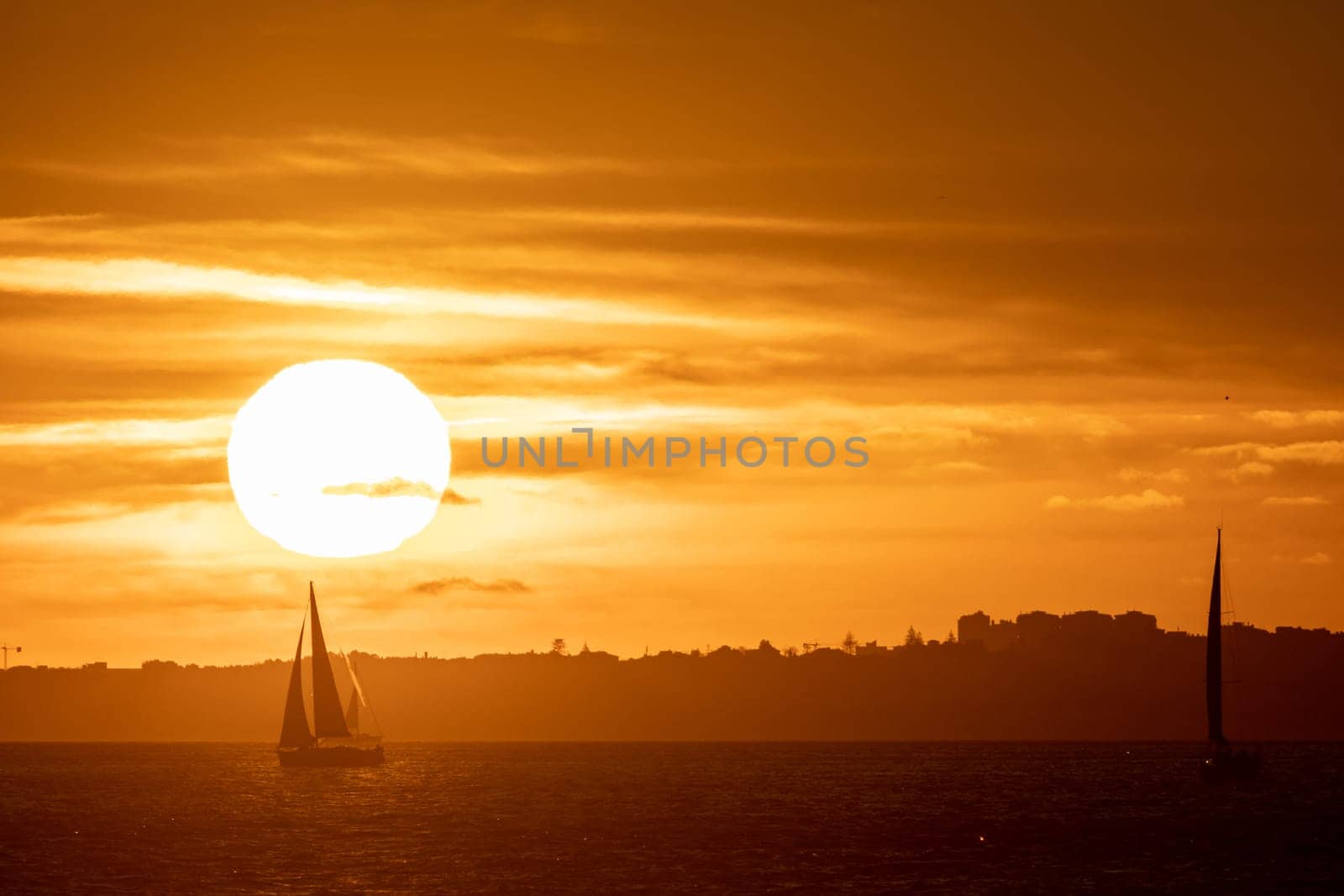 Sailing boats float in the sea at a bright orange sunset. Mid shot