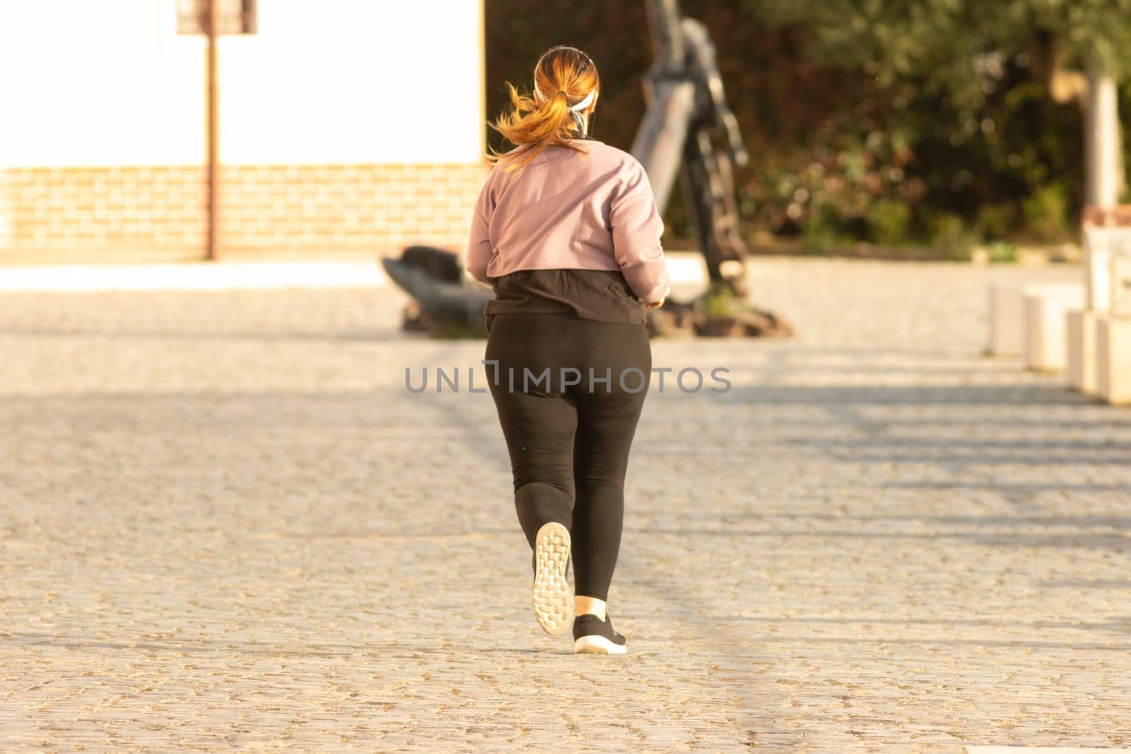 Plump girl jogging on the street. Mid shot