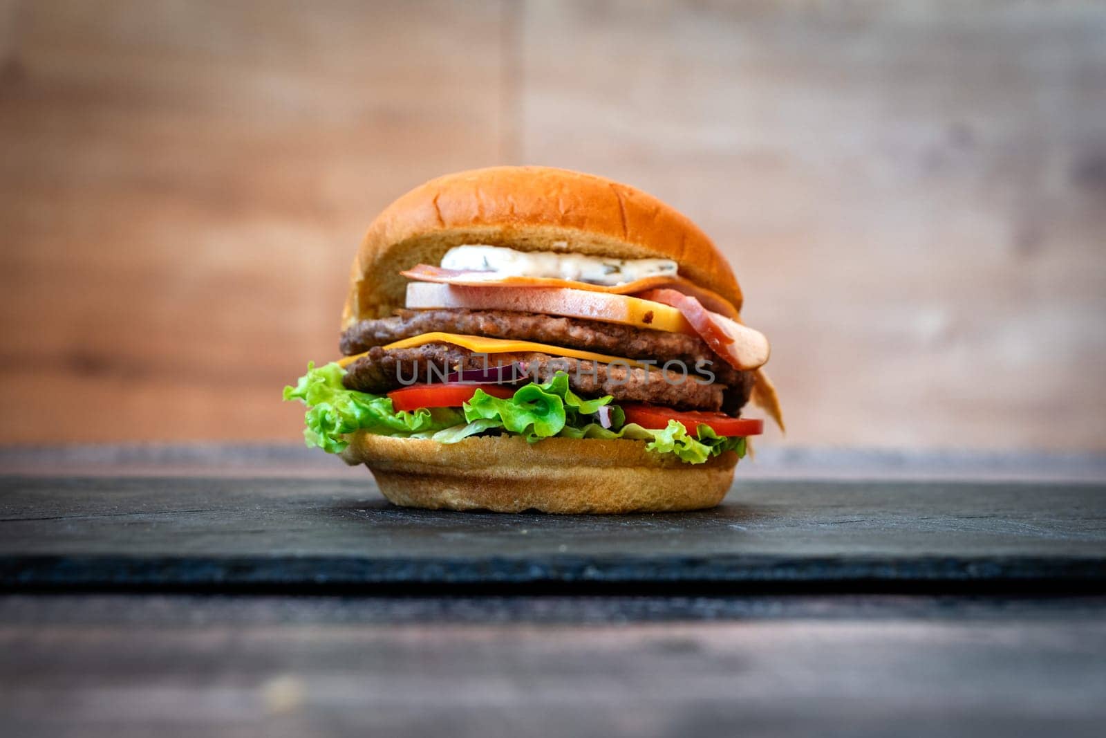 beef burger with sesame lettuce bun tomato cheddar cheese on black background