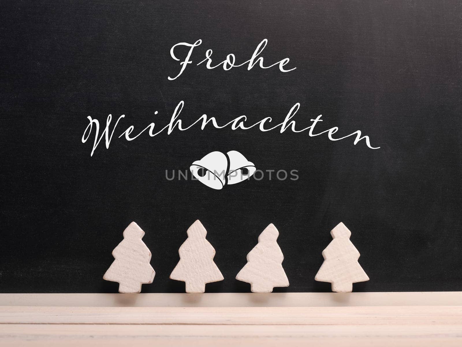Chalkboard with the German inscription Merry Christmas and decorative wooeden tree shapes