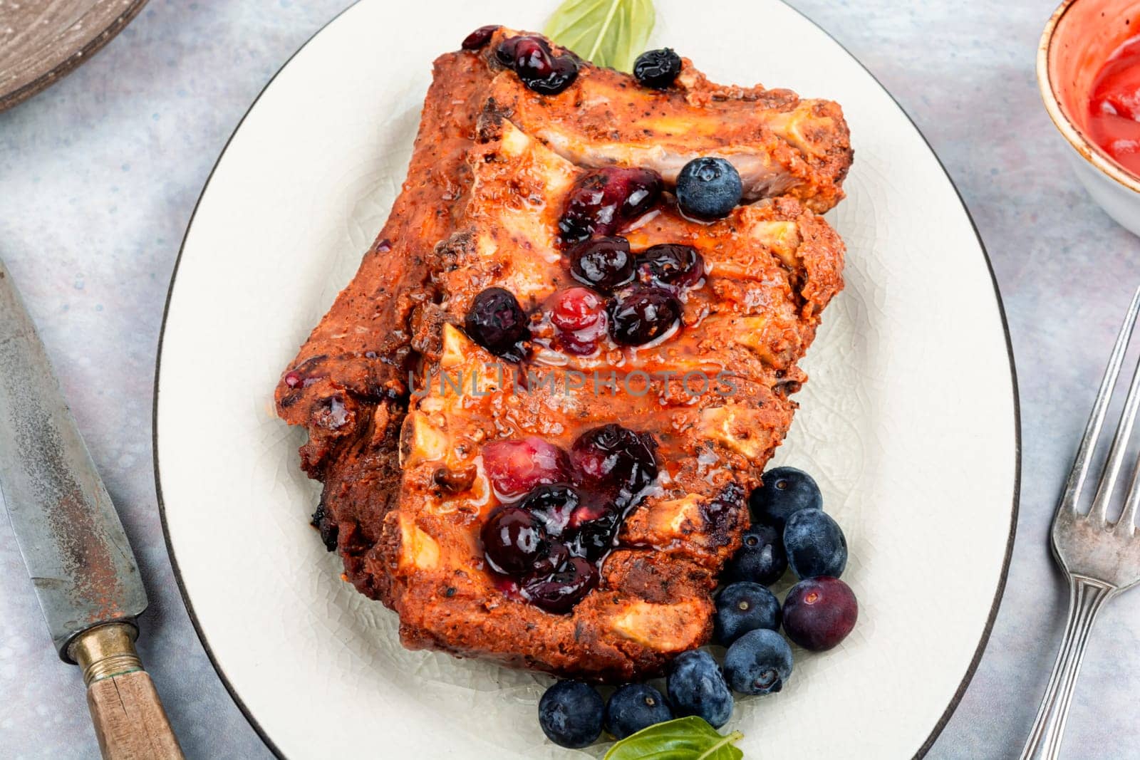 Fried pork ribs with blueberry sauce on a stone background