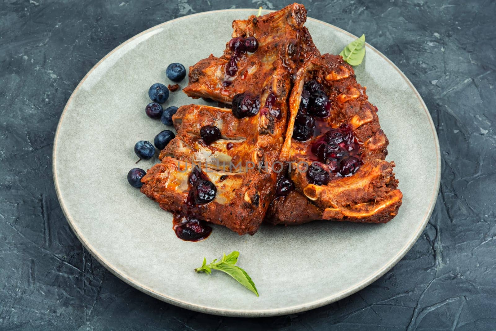 Fried pork ribs with blueberry sauce on a stone background