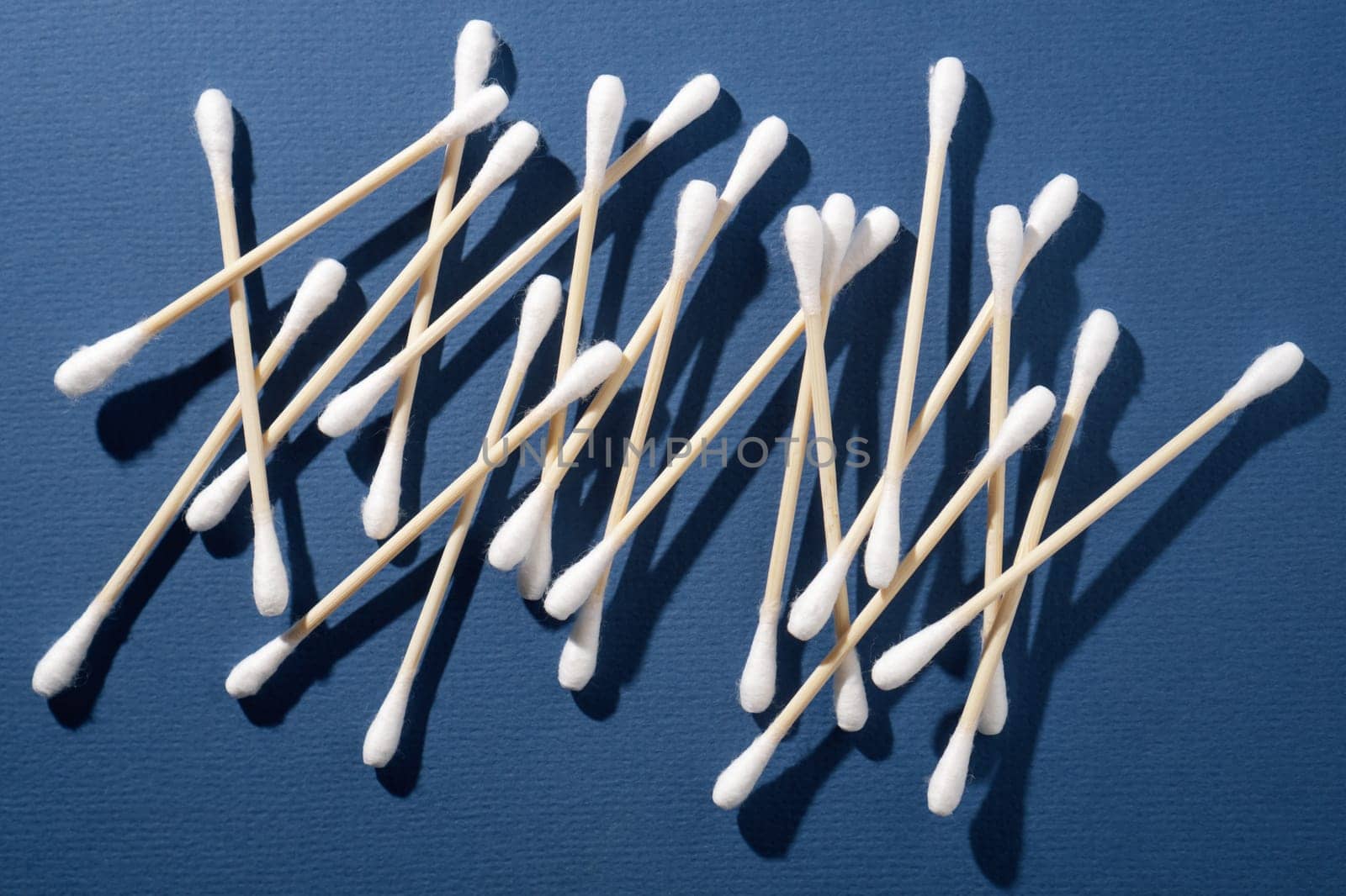 Bunch of disposable soft cotton buds with beige stick of bamboo, using for artificial eyelash extension procedure, lying against dark blue background. Clean tools for creating fashionable look.