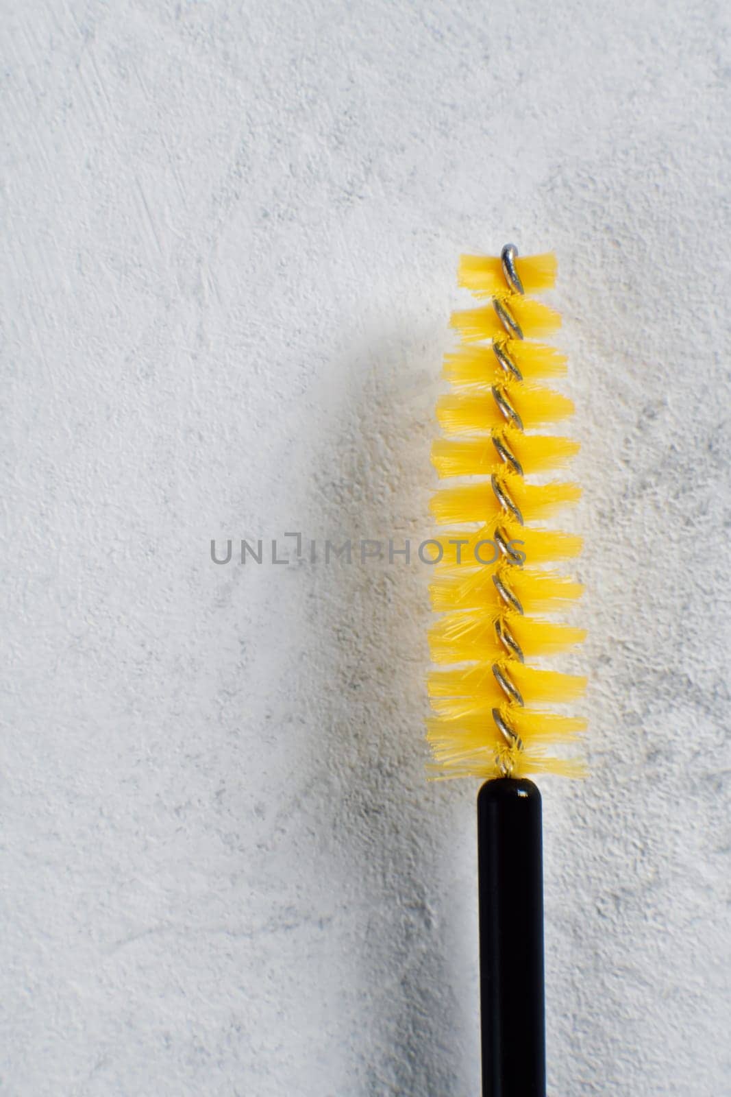 Yellow disposable eyelash extension brush isolated against white wall. Tool with fine bristles allowing for precise and controlled lash placement, ensuring achievement flawless result. Vertical.