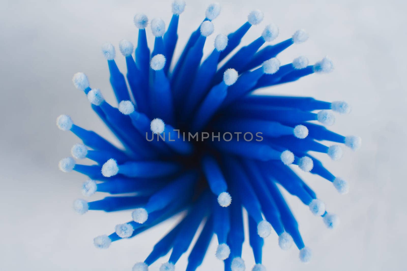 View from above of bunch of professional microbrushes with blue stick, using for eyelash extension procedure, applying material on cilia, lying in container and creating image of delicate flower.