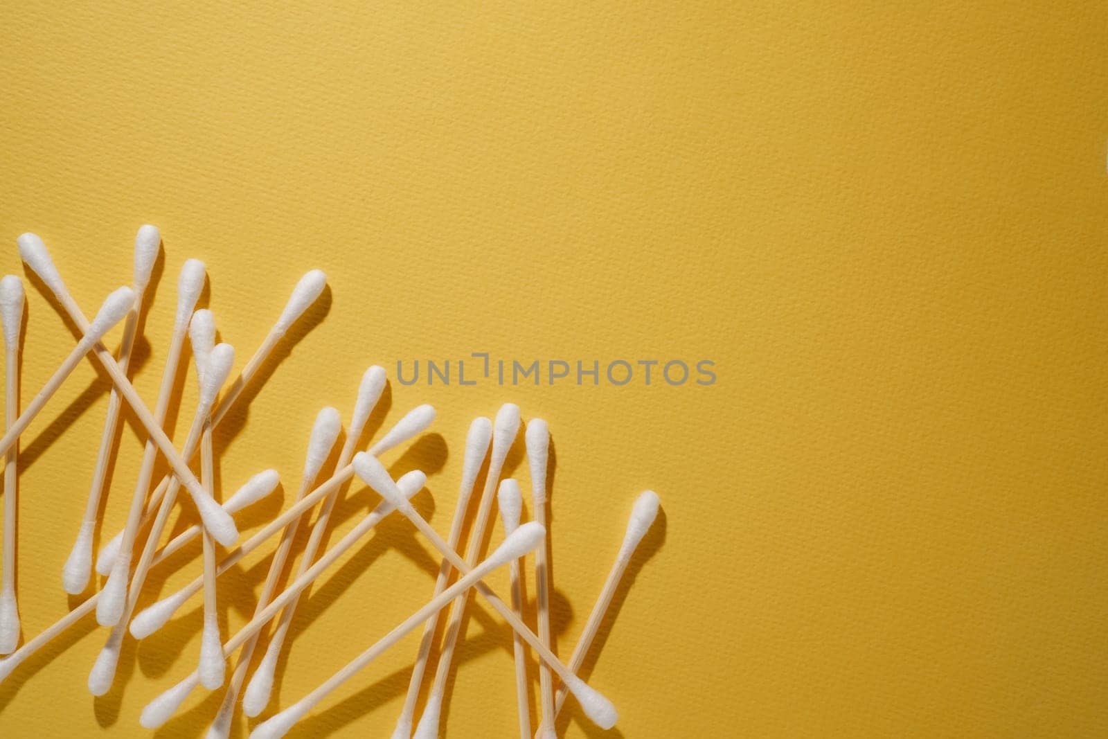 Bunch of disposable cotton buds with beige bamboo sticks isolated on bright yellow background, positioning in left lower corner. Consumable using for assisting throughout cilia extension procedure.