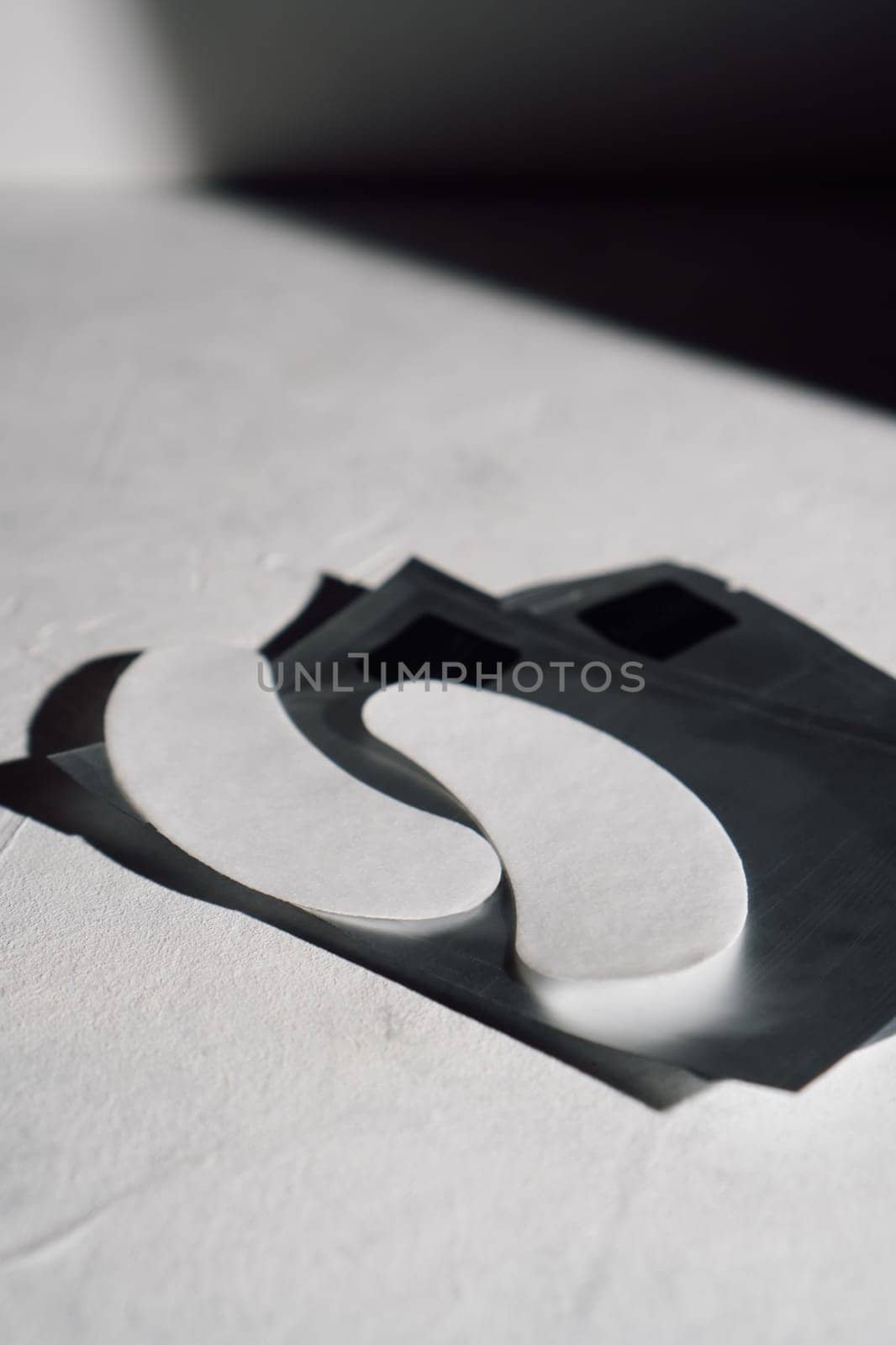 White disposable eyelash extension patches for insulating lashes, applied on lower eyelids in process of procedure lying on black wrapping on clean desk. Vertical.