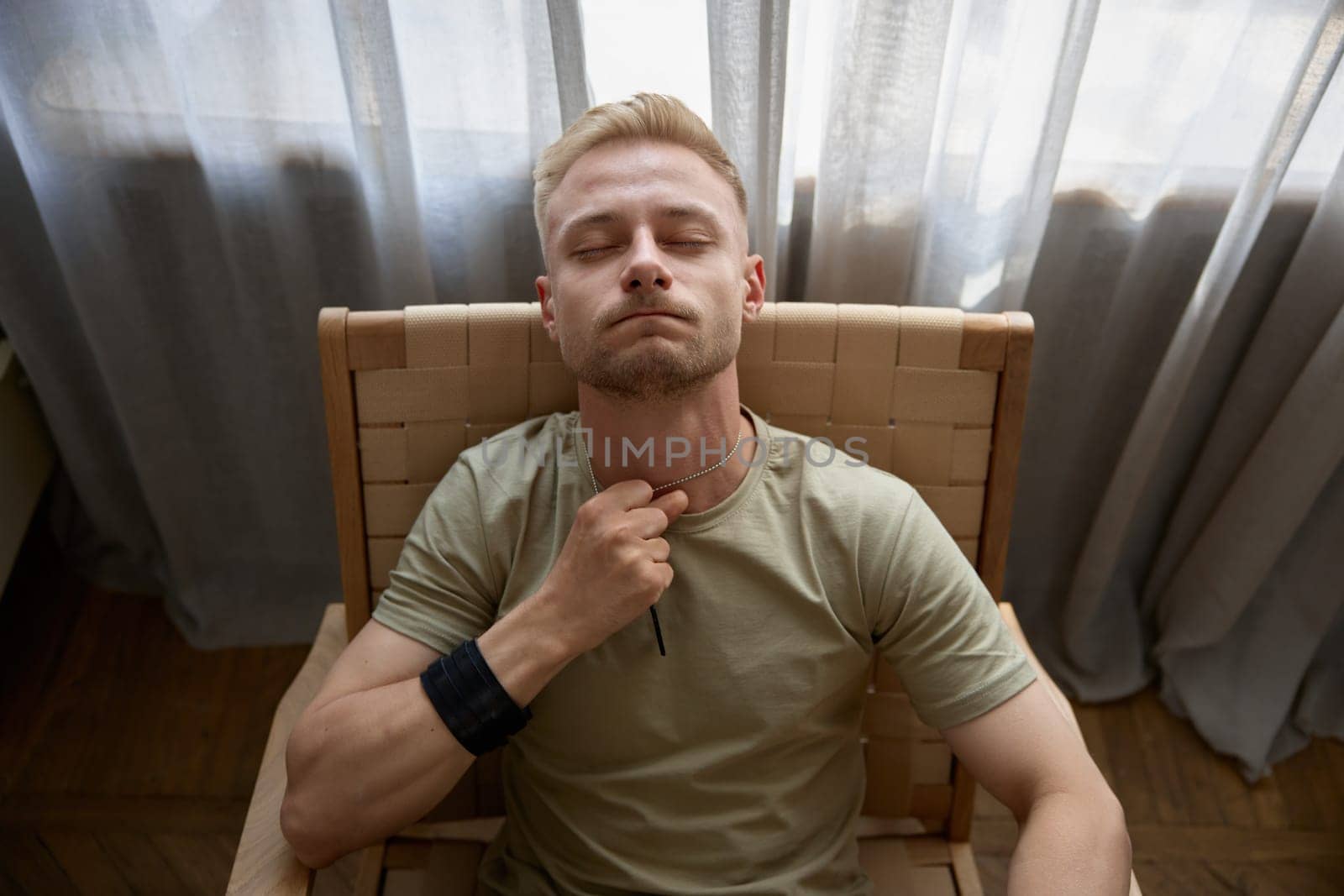Depressed lonely man soldier with emotional problem and war syndrome feeling nervous, suffering from PTSD touching his badge tag sitting on chair alone at home