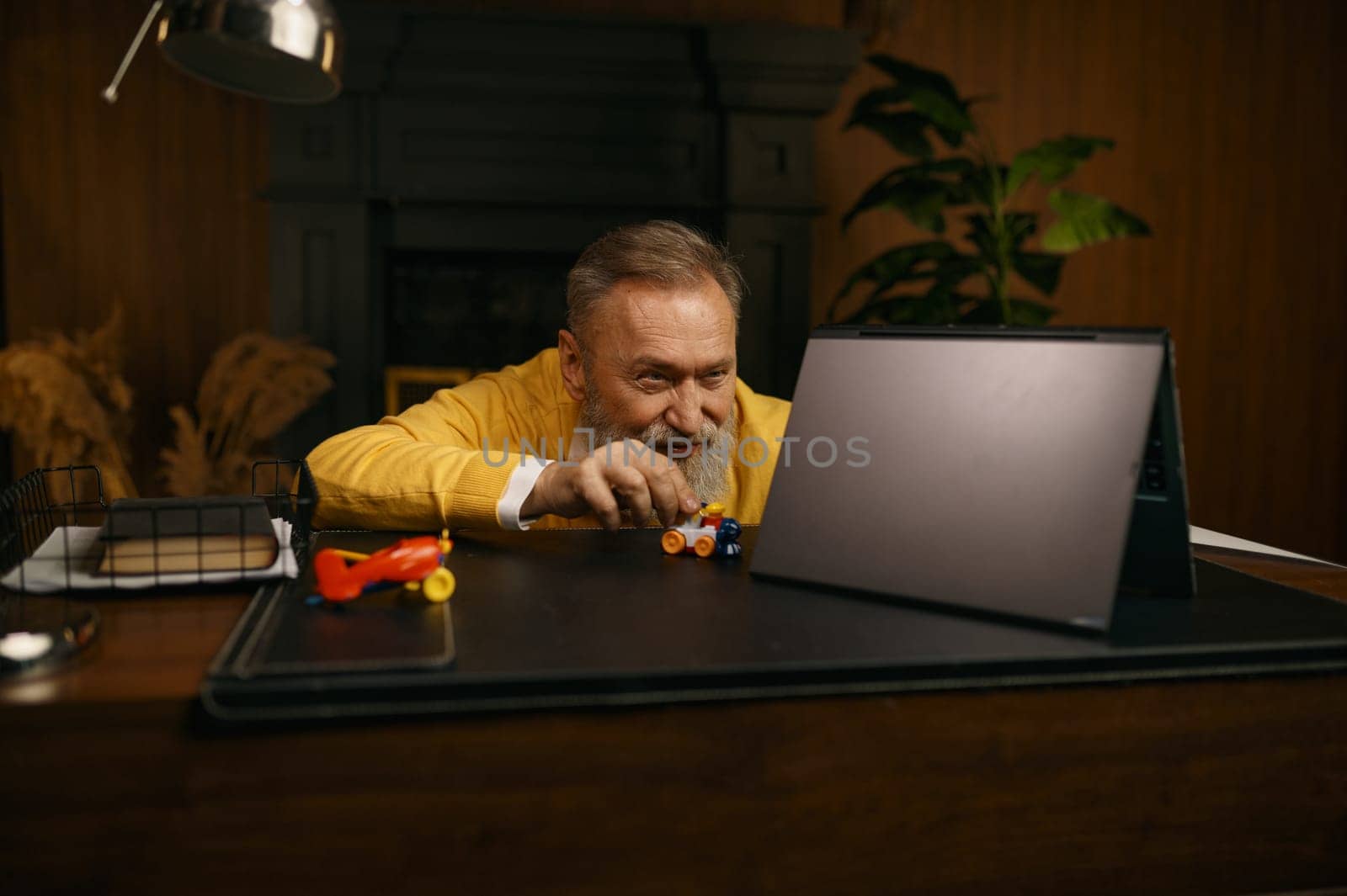 Senior man playing toys at workplace having fun after hard work in home office. Older employee accountant taking break time enjoying train race gaming