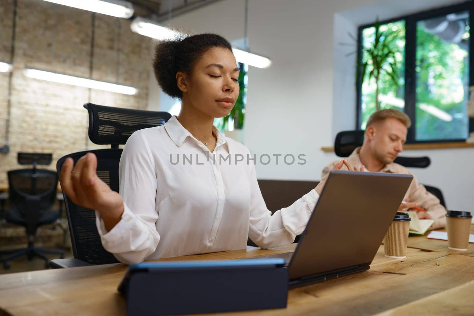 Businesswoman office worker relaxing doing yoga sitting front of laptop computer at coworking open space