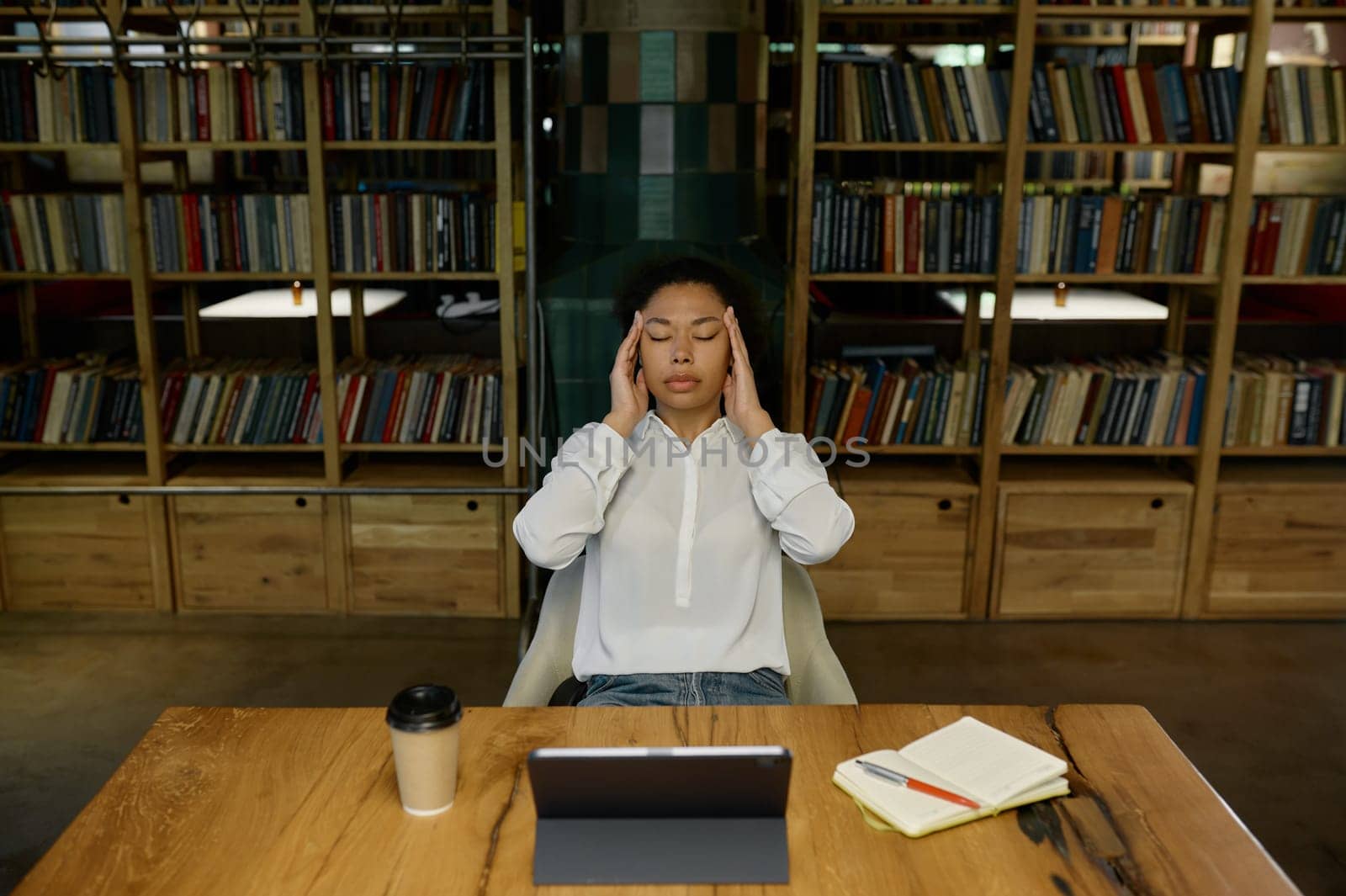 Tired overworked female office worker touching head massaging temples suffering from headache or tension while sitting at desk table front of computer