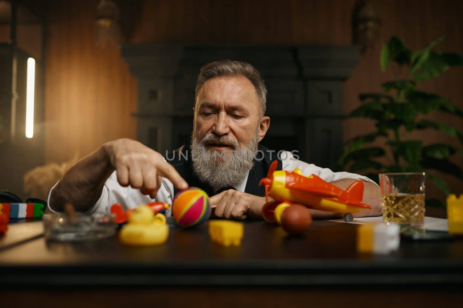 Portrait of thoughtful senior businessman playing toys while rest at workplace in home office. Elderly male having fun enjoying stress relief entertainment