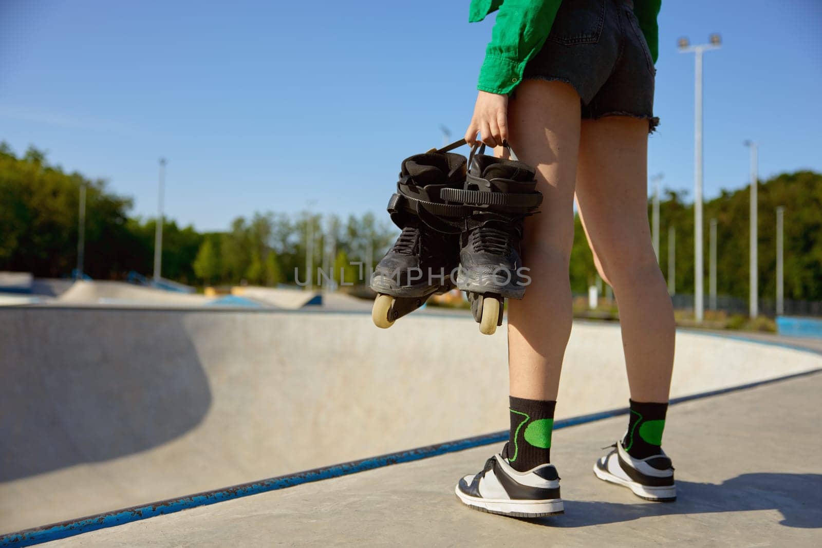 Closeup female teenager with rollers standing front of skating ramp. Preparation for sports training with professional equipment