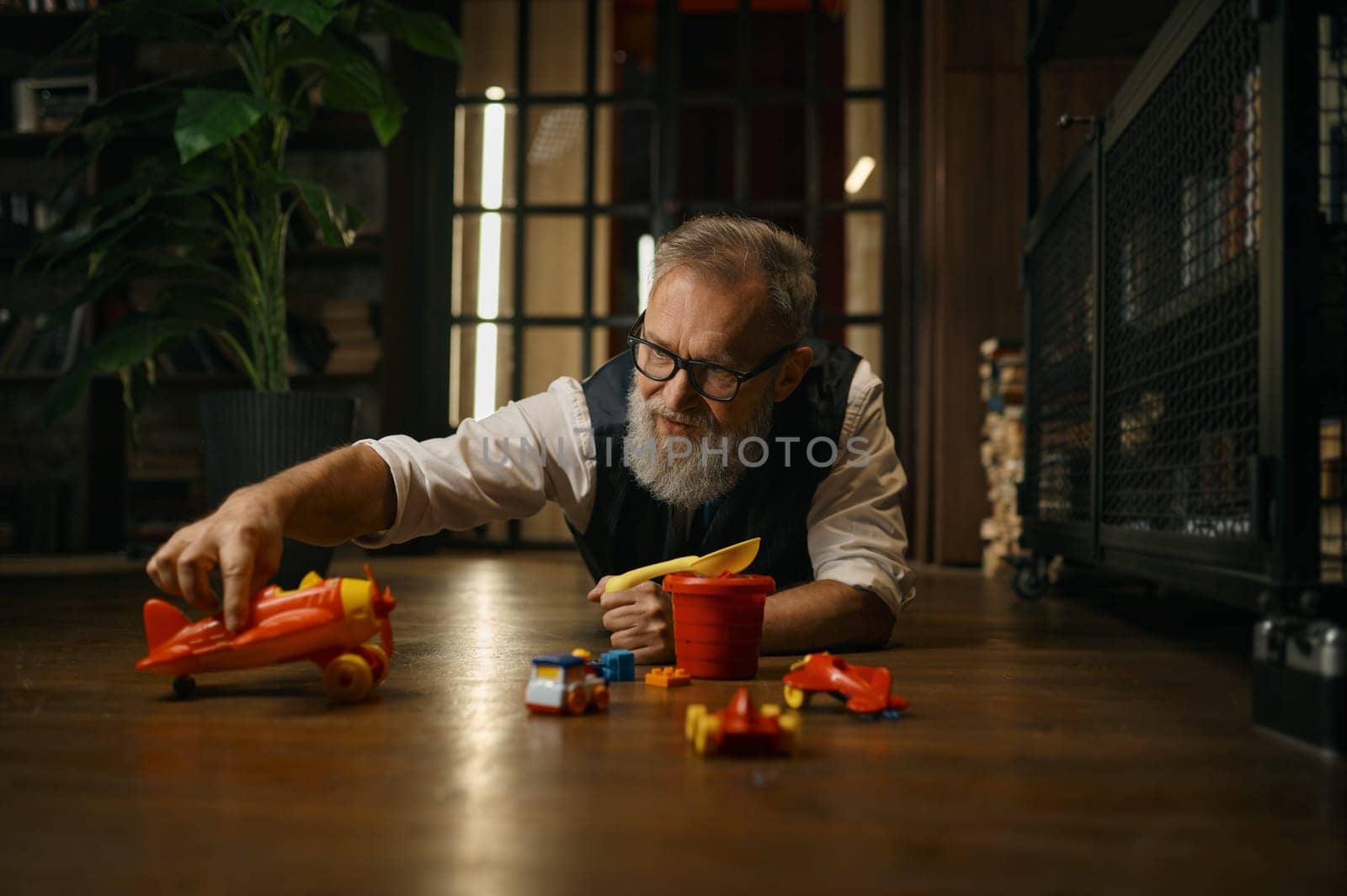 Funny successful senior businessman playing toys while lying on floor at home office. Relax time after work concept