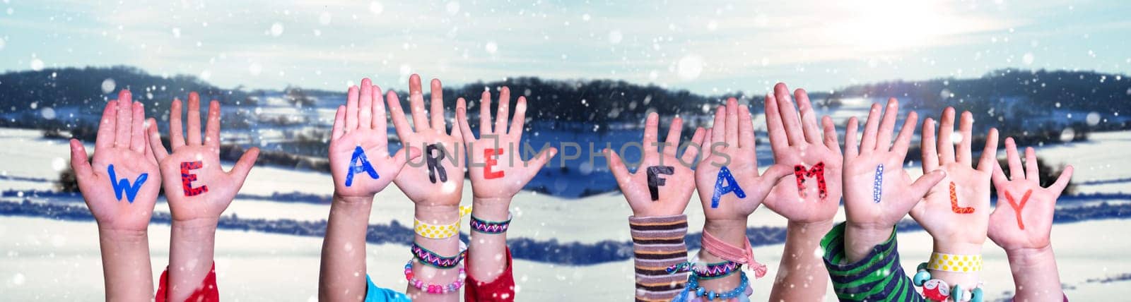 Children Hands Building Colorful English Word We Are Family. White Winter Background With Snowflakes And Snowy Landscape.