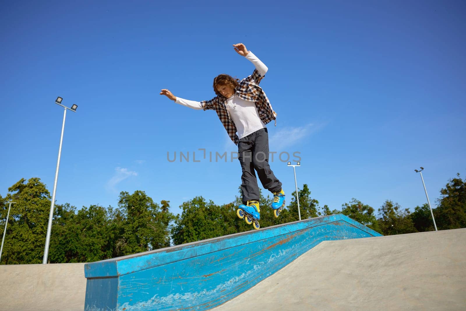 Young teen wearing inline skates doing balancing stunt at skateboard park. Extreme sports event for teenagers